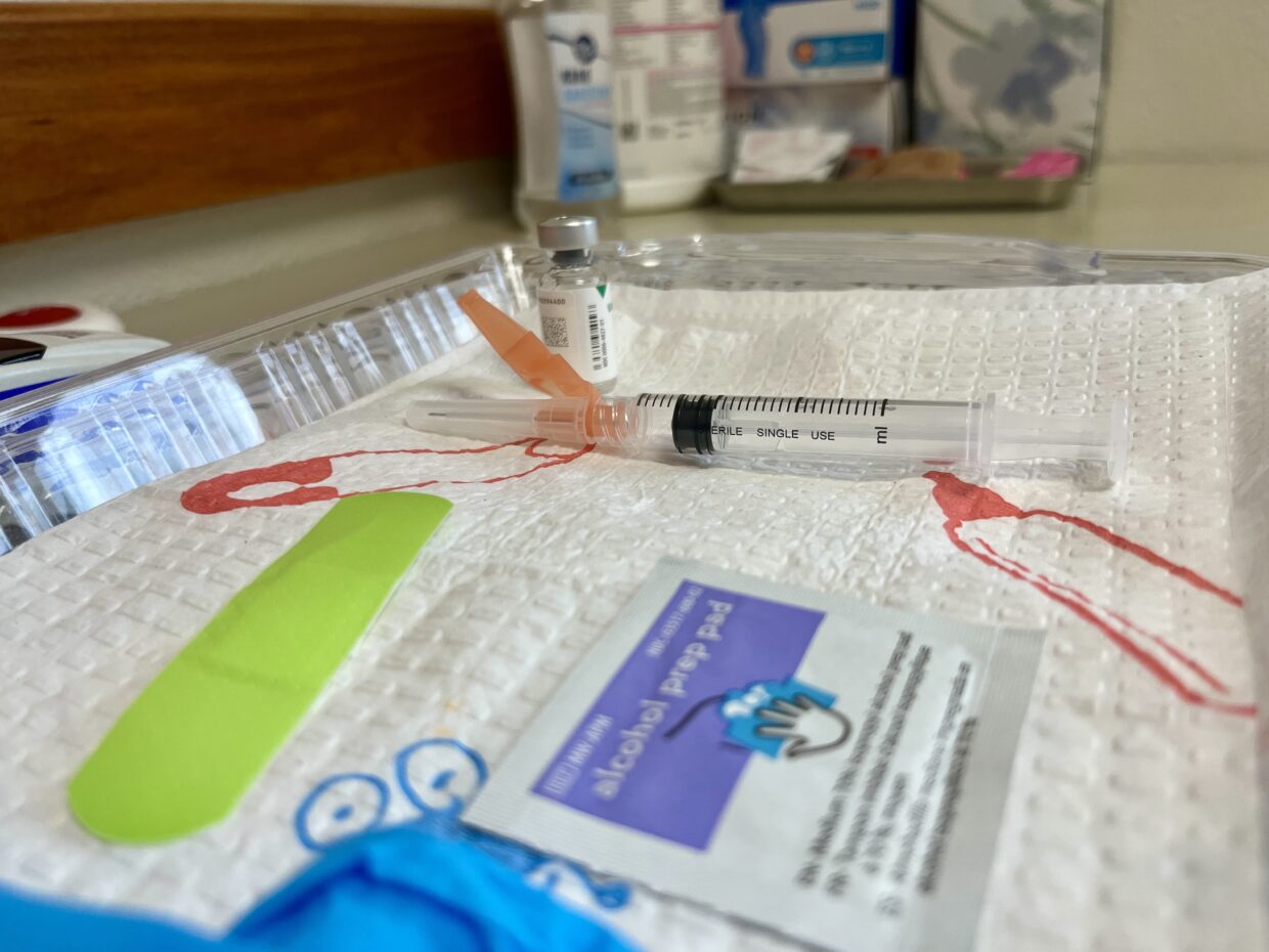 Nurse's tray with vaccine, syringe, prep pad, and bandage.